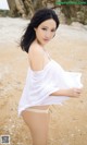 A woman in a white shirt is standing on a beach.