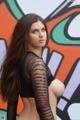 A woman with long brown hair standing in front of a graffiti wall.