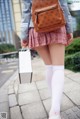 A woman in a skirt and white socks holding a brown bag.