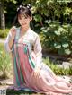 A woman in a pink and blue hanbok sitting on the grass.