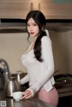 A woman standing in a kitchen next to a kettle.