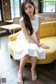 A woman in a white dress sitting on a yellow couch.